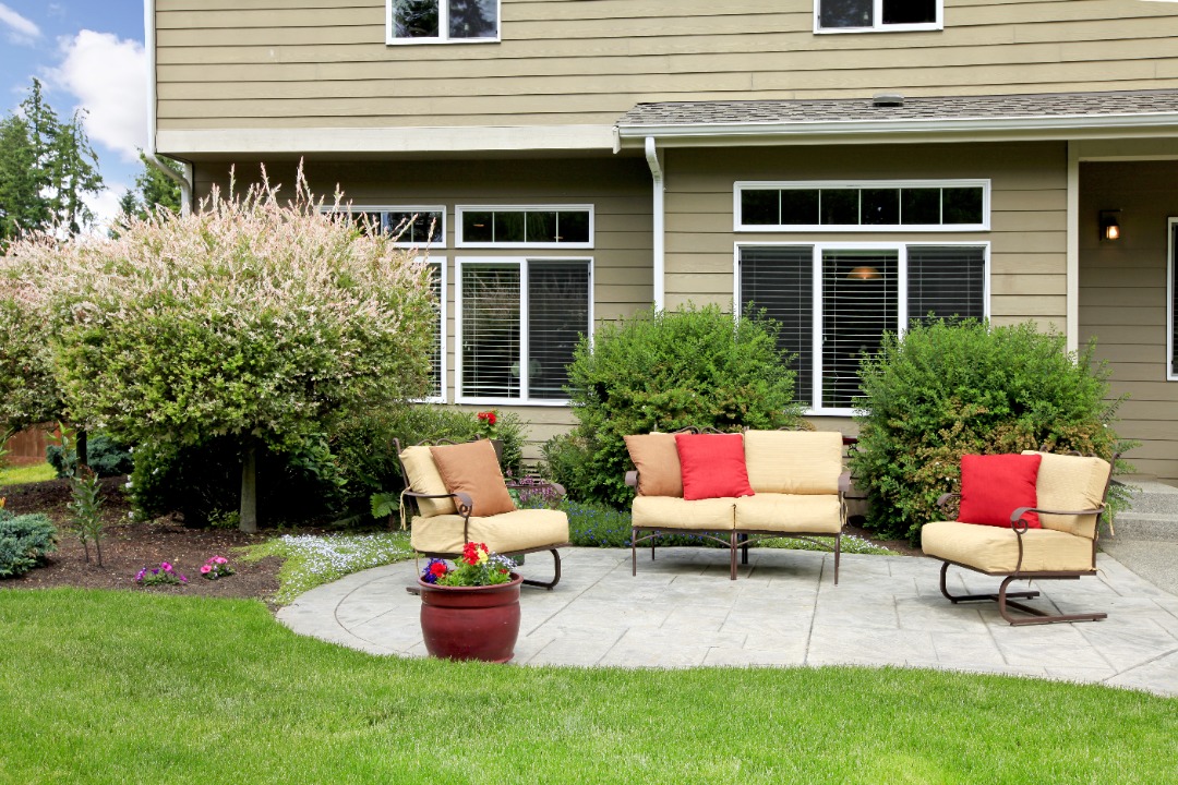 Spacious backyard with gazebo, colorful potted flowers, outdoor grill, and seating area on a multi-level stone patio.