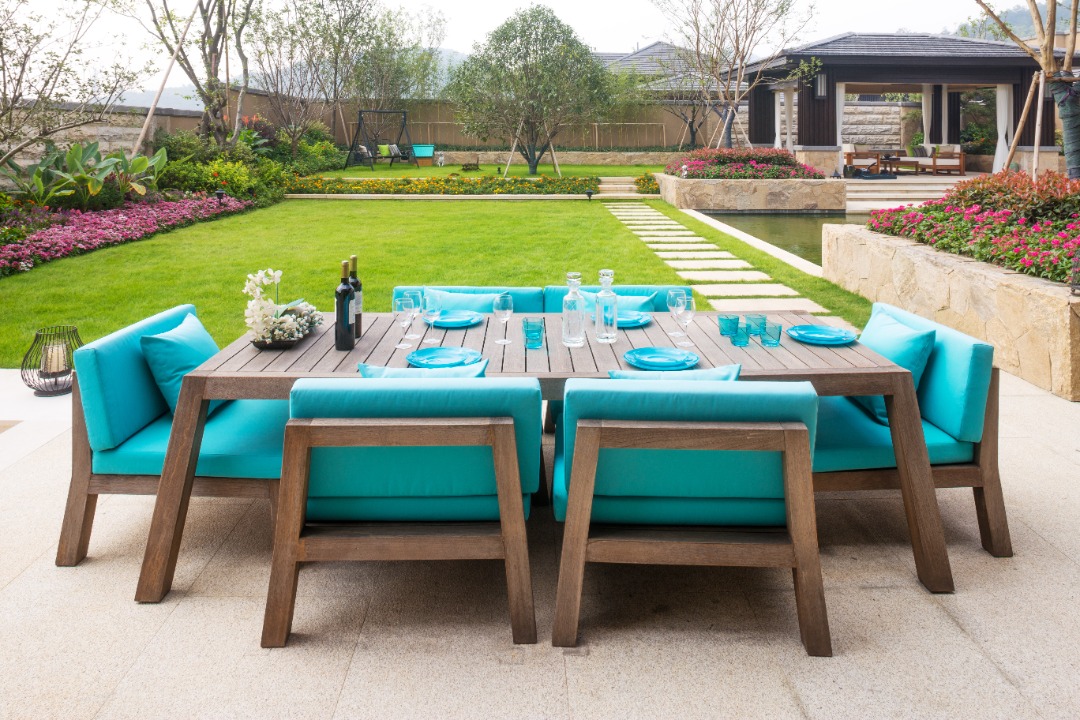 Modern patio dining set with turquoise cushions on a tiled terrace overlooking landscaped garden and manicured lawn.