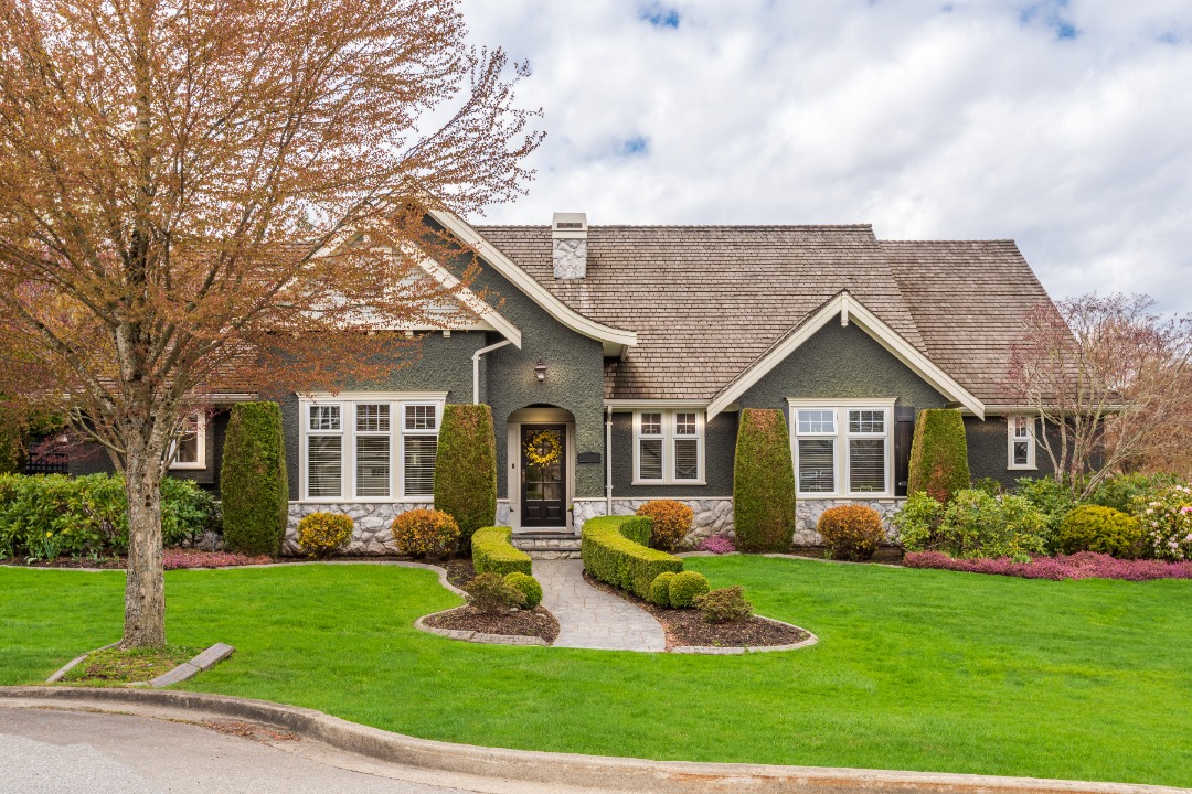 Charming craftsman-style house with manicured lawn, shaped hedges, and symmetrical foundation planting along the facade.