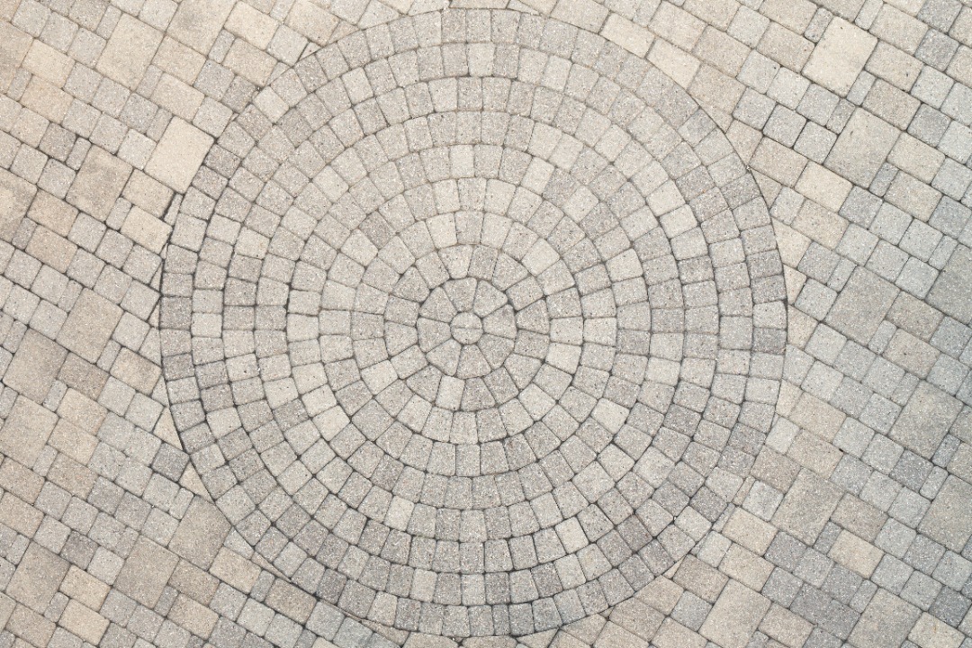 Circular paver design with concentric stone pattern set into square paver field, creating a focal point in patio flooring.