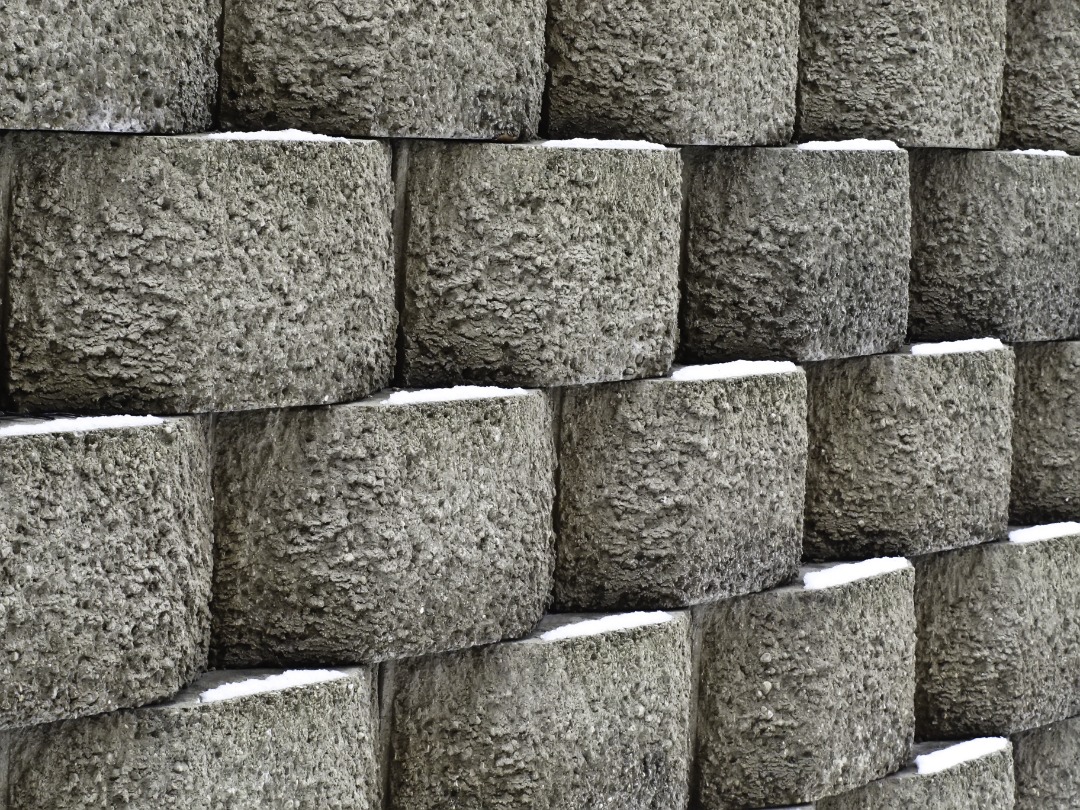 Close-up of textured concrete retaining wall blocks with staggered alignment, showing snow buildup between block layers.