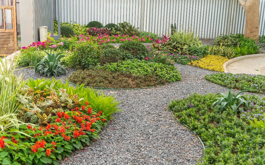 Curved gravel paths wind through vibrant, circular garden beds with colorful flowers, shrubs, and tropical plants.